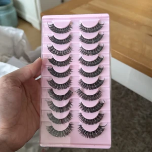 Set med lösögonfransar - Säljer ett set med 10 par dramatiska lösögonfransar. Perfekta för att ge dina ögon en intensiv look. Fransarna är täta och långa, vilket ger en fyllig effekt. De kommer i en praktisk rosa förpackning som håller dem organiserade.