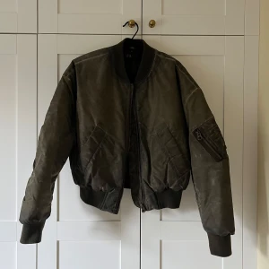 Olivgrön bomberjacka från Zara - Snygg olivgrön bomberjacka från Zara med dragkedja framtill och ribbade muddar. Jackan har en klassisk bomberstil med fickor och en ärmficka med dragkedja. Perfekt för en cool och avslappnad look. Storlek L men passar bättre en storlek S - M! 