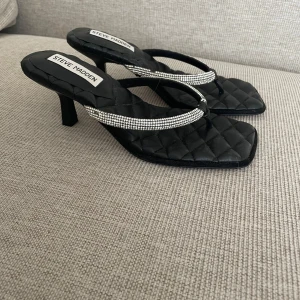 Svarta klackar från Steve Madden - Snygga svarta klackar från Steve Madden med quiltad sula och glittriga remmar. Perfekta för en kväll ute eller en speciell tillställning. De har en fyrkantig tå och en elegant design som ger en lyxig känsla.