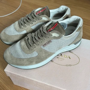 Gröna/beige sneakers från Prada - Snygga grön-beige sneakers från Prada med en kombination av mocka och mesh. Skorna har en rund tå och snörning framtill. Perfekta för en stilren och avslappnad look. Använda med kärlek. Köpta i Danmark för 5 år sedan. Storlek 5 i UK storlek, dvs 39 i Europa. Skulle säga att de passar 38.5, 39 och 39.5. Se bilder för skick.