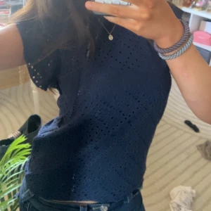 Mörkblå blus - Säljer en snygg mörkblå blus med korta ärmar och ett diskret hålmönster. Perfekt för en stilren look. Blusen har en normal passform och är tillverkad i ett lätt material som passar bra till både jeans och kjol.