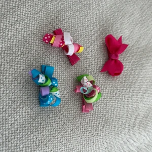 Färgglada hårspänne med rosetter - Säljer ett set med fyra färgglada hårspänne dekorerade med rosetter. hårspänne har olika färger och mönster, inklusive prickiga och randiga detaljer. Perfekta för att liva upp vilken frisyr som helst!