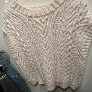 Vit stickad väst från H&M - Säljer en mysig vit stickad väst från H&M med ett snyggt flätmönster på framsidan. Västen har en ribbad krage och är perfekt för lager-på-lager-stil. Passar utmärkt till både jeans och kjol.