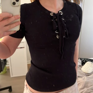 Svart ribbad topp från Sleek Chic - Snygg svart ribbad topp från Sleek Chic med snörning framtill. Perfekt för en stilren look. Kortärmad och i ett stretchigt material som ger en bekväm passform. Typ storlek S