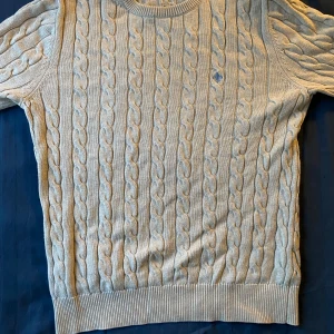 Beige kabelstickad tröja från Morris - Säljer en beige kabelstickad tröja från Morris i 100% bomull, strl S. Tröjan har långa ärmar, rund halsringning och en liten broderad logga på bröstet. Nypris 1200kr. 