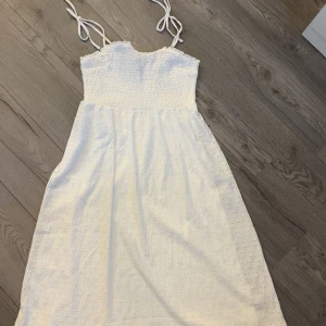 Vit sommarklänning från H&M Divided - Söt vit klänning från H&M Divided med smock upptill och tunna axelband. Klänningen har broderade detaljer och är i lätt, luftig bomull – perfekt för varma dagar. Längden är mellan knä och vad.