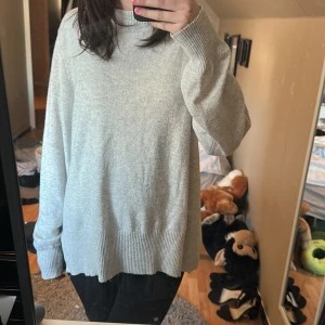 Ljusgrå stickad tröja med polokrage - Mysig ljusgrå stickad tröja med polokrage och långa ärmar. Tröjan har en oversized passform och breda ribbade muddar vid ärmslut och nederkant. Perfekt för lager-på-lager och chill dagar. Fläcken har inte testas att få bort!