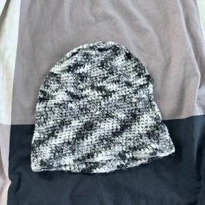 Gråmelerad stickad mössa - Säljer en gråmelerad stickad mössa med grov struktur. Mössan har en mjuk och fluffig känsla och passar perfekt för kyliga dagar. Färgen är en mix av olika grå nyanser vilket ger ett unikt utseende.