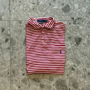 Röd- och vitrandig pikétröja från Polo Ralph Lauren - Säljer en klassisk pikétröja från Polo Ralph Lauren i rött och vitt randigt mönster. Matrialet är bomull och nypriset ligger på cirka 1500