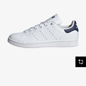 Adidas Stan Smith  - Klassiska vita Adidas Stan Smith sneakers med marinblå detalj på hälen. Skorna har en stilren design med perforerade ränder på sidorna och snörning framtill. Perfekta för en clean och tidlös look.