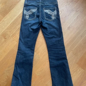 Mörkblå bootcut jeans från Gina Tricot - Säljer ett par mörkblå jeansbyxor från Gina Tricot med snygga broderade detaljer och paljetter på bakfickorna. Byxorna är bootcut och lågmidjade. Jag är 164 cm och dom passar perfekt i längd! Har inte använt dom mycket men 3-4 st paljetter på baksidan har åkt av. 💗💗