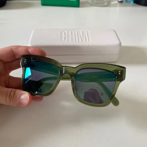 Gröna solglasögon från CHIMI - Snygga solglasögon från CHIMI i modellen #005. Glasögonen har en transparent grön båge och mörka spegelglas. Klassisk fyrkantig form som ger en cool look. Perfekt accessoar för soliga dagar.