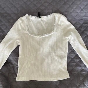 Vit ribbad långärmad topp från H&M Divided - Säljer en vit ribbad långärmad topp från H&M Divided. Toppen har en fyrkantig ringning med spetsdetalj runt halsen. Säljer en likadan i grå