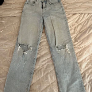 Ljusblå slitna jeans från Ginatricot  - Ljusblå jeans med raka ben och slitningar på båda knäna från Ginatricot. Klassisk femficksmodell med knapp och dragkedja i gylfen. Perfekta för en avslappnad och trendig look.