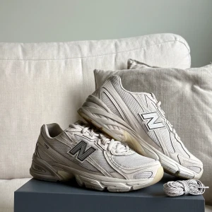 New Balance 740 - Säljer ett par stilrena beige/vita New Balance 740 sneakers med mesh och syntetpaneler. Skorna har klassisk N-logga på sidan, rund tå och platt sula. Perfekta för dig som gillar en clean och sportig look. Skosnören i matchande färg medföljer. Använda två gånger