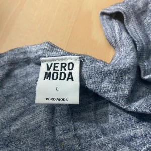 Grå långärmad topp från Vero Moda - Säljer en grå långärmad topp från Vero Moda med volangdetalj nedtill. Mjuk och skön, perfekt till vardags. Liten v-ringning framtill och avslappnad passform.