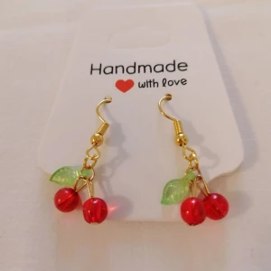 Handgjorda körsbärsörhängen med guldfärgade detaljer - Söta örhängen med körsbärsdetaljer i rött och grönt, hängande på guldfärgade krokar. Perfekta för att ge en lekfull touch till din stil. Handgjorda och unika!
