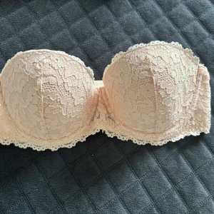 Ljusrosa axelbandslös spets-bh från Dare - Säljer en ljusrosa axelbandslös bh från Dare /lindex med vacker blommig spets och lätt vadderade kupor. Perfekt under toppar och klänningar där du vill ha axlarna fria. Fina spetsdetaljer längs kanterna för en extra feminin look.