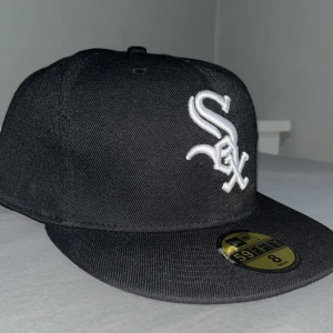 Svart keps från New Era - Svart keps från New Era 59FIFTY med Chicago White Sox-logga. Använde ej den va stor så den är i ny skick. Perfekt nu till sommaren. Pris kan diskuteras. Storlek 8 eller 64cm