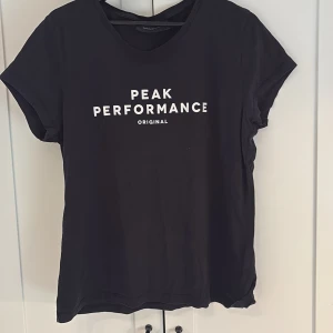 Svart t-shirt från Peak Performance - Svart t-shirt från Peak Performance med vit text på bröstet. Klassisk rund halsringning och korta ärmar. Perfekt basic-plagg med stilren design och mjukt material.