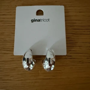 Silverfärgade örhängen från Gina Tricot - Säljer ett par stilrena, chunky örhängen i silverfärg från Gina Tricot. De har en rundad, något droppformad design som ger ett modernt och trendigt intryck. Perfekta för att lyfta vilken outfit som helst. Helt oanvända, men de gick inte att lämna tillbaka i butik så får sälja. 