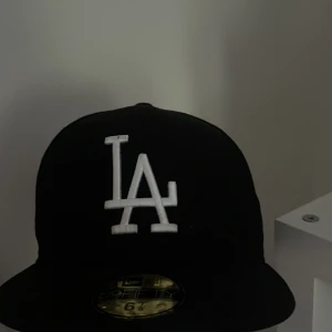 Svart LA Dodgers keps från New Era - Säljer en svart keps från New Era med LA Dodgers-logga framtill i vitt. Kepsen har broderade märken på sidorna för World Series och Anniversary, samt en ljusblå undersida på skärmen. Klassisk 59FIFTY-modell.