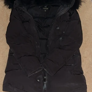 Svart dunjacka från CECION - Säljer en svart dunjacka från CECION med huva och svartpäls. Jackan har dragkedja framtill och flera fickor. Perfekt för kalla dagar och har en klassisk, stilren look. Avdragbar päls. Använt ett fåtal gånger! 