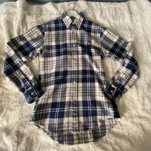 Rutig skjorta från Polo Ralph Lauren - Snygg rutig skjorta från Polo Ralph Lauren i blått och vitt. Skjortan har klassisk krage, knappar framtill och långa ärmar. Tillverkad i mjuk bomull och har en custom fit-passform. Perfekt för dig som gillar stilrena mönster. Aldrig använd. Topp skick, prislapp och äktighetsbevis finns. Intresserad? Bara att hojta till!! 
