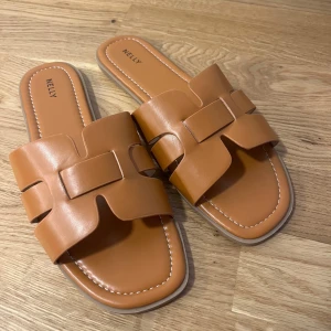 Bruna sandaler från Nelly - Snygga bruna sandaler från Nelly med öppen tå och breda remmar i syntetmaterial. Helt oanvända.