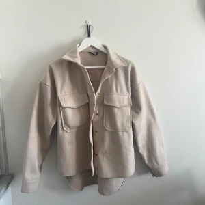 Beige overshirt med fickor - Snygg beige overshirt med stora bröstfickor och knappar framtill. Skjortan har lång ärm och en avslappnad passform, perfekt att slänga över en t-shirt. Materialet känns mjukt och lite tjockare, vilket gör den extra mysig.