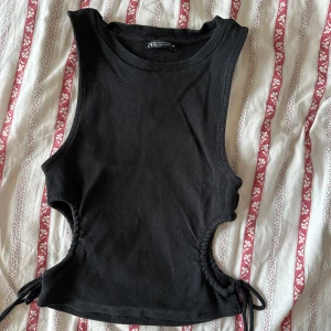 Svart topp - Snygg svart topp från Zara. I bra skick, använd några gånger. Snygg knytningsdetalj i sidan. Storlek M. 
