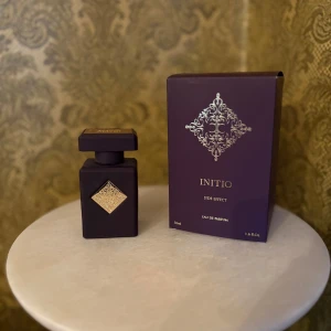 Initio Side Effect Eau de Parfum - Lyxig parfymflaska från Initio i mörklila med guldfärgad detalj och matchande ask. Flaskan har en fyrkantig form och elegant design, perfekt för dig som gillar exklusiva dofter. NÄSTAN HELT NY 