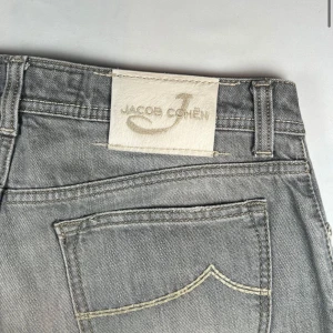   Jacob Cohën jeans w34 lenght 112 - Riktigt feta  grå jeans från Jacob Cohën med klassisk femficksdesign och ljusa slitningar. Jeansen har raka ben och silverfärgad knapp framtill. Perfekta för en stilren och avslappnad look. W34 lenght 112 