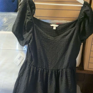 Svart klänning med puffärmar - Säljer en svart klänning med v-ringning och puffiga kortärmar. Klänningen har en lätt rynkad struktur och markerad midja för en feminin siluett. Perfekt för dig som gillar enkel men trendig stil.