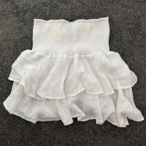 Vit volangkjol  - Supersöt vit kortkjol, dubbla volanger. Kjolen är luftig och lätt, perfekt för varma dagar. Enkel att matcha med olika toppar.