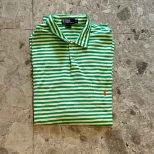 Grön- och vitrandig pikétröja från Polo Ralph Lauren - Säljer en klassisk pikétröja från Polo Ralph Lauren i grönt och vitt randigt mönster. Tillverkad i 100% bomull. Nypriset ligger på cirka 1500kr