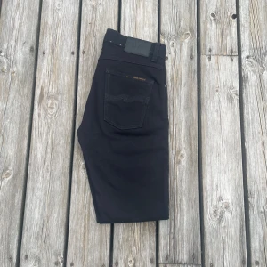 Svarta jeans från Nudie Jeans - Säljer ett par svarta jeans från Nudie Jeans med klassisk bakficka och diskret logga. Jeansen har raka ben och normal passform, perfekta för en stilren look. Materialet är mjukt och bekvämt, och de har en snygg svart färg. Modellen är Lean Dean. Nypris är ungefär 1600kr!