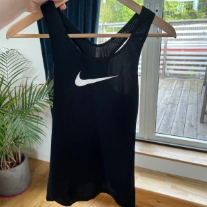 Svart träningstopp från Nike Pro - Säljer en svart träningstopp från Nike Pro med klassisk vit logga framtill. Toppen är ärmlös och har meshdetaljer upptill för extra ventilation. Perfekt för intensiva träningspass eller gymmet.