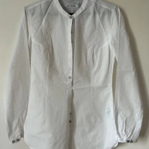 Vit skjorta från The Shirt Factory - Klassisk vit skjorta från The Shirt Factory. Skjortan har lång ärm, knappar framtill och en stilren, rundad krage. Skjortan är dessutom i väldigt bra skick och bara använts en gång.