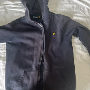 Svart hoodie från Lyle & Scott Junior - Mörkgrå hoodie med dragkedja från Lyle & Scott Junior. Klassisk design