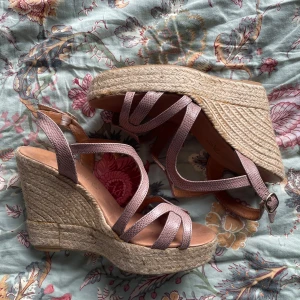 Rosa kilklackssandaler med flätad sula - Snygga rosa sandaler med kilklack och flätad sula. De har flera remmar i ett orm skinn liknande material och en justerbar rem runt ankeln. Använda ett par gånger men i fint skick! :) 