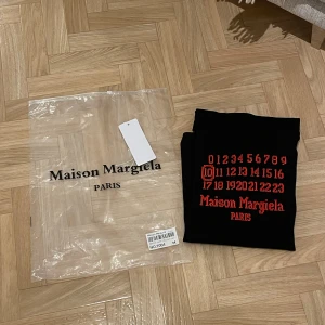 Svart t-shirt från Maison Margiela - Säljer en svart t-shirt från Maison Margiela med röd text och siffror på framsidan. Den passade inte mig alltså inget tecken på användning.