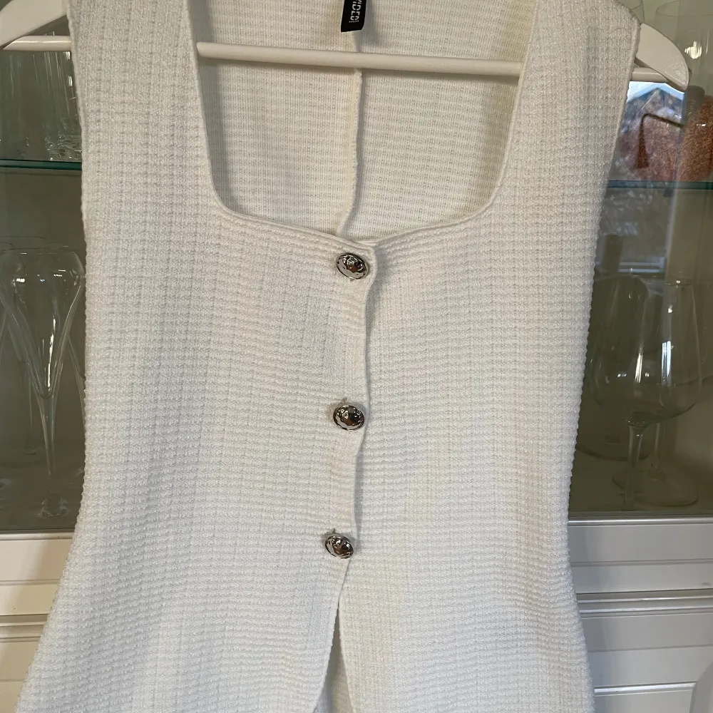 Snygg vit topp från H&M med tre dekorativa knappar framtill. Västen har en elegant och stilren design, perfekt för att lyfta vilken outfit som helst. Helt ny men saknar lapp, säljer då den var för stor🤍. Yläosat.