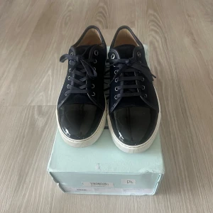 Svarta sneakers från Lanvin - Snygga svarta sneakers från Lanvin med en glansig tå och snörning. Skorna har en vit sula som ger en fin kontrast till det svarta. Perfekta för en stilren look. Storlek 42 ar som 43.