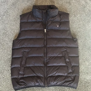 Svart dunväst från GANT - Snygg svart dunväst från GANT med dragkedja framtill. Otroligt bra skick, som ni kan se! Bara använd ett par gånger. Säljer billigare för vill ha den såld snabbt!