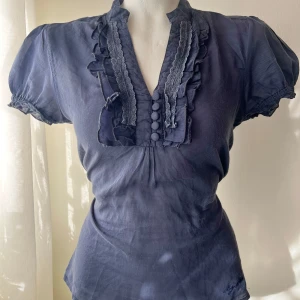 Topp - Mörkblå kortärmad skjorta med puffiga ärmar. Den har tecken på användning, som små slitningar vilket syns i några av bilderna. Storlek S, går att knyta i midjan.