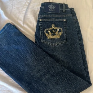 Mörkblå crown jeans  - Snygga mörkblå jeans med en broderad krona i guld på bakfickan. Jeansen har en klassisk femficksdesign och en knappgylf. Perfekta för en stilren look.Dem är från Crown jeans och knappt använda 