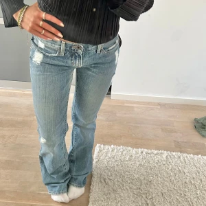 Blå bootcut jeans med slitningar - Snygga blå bootcut jeans med slitningar och broderade detaljer på bakfickorna. Jeansen har en låg midja och en klassisk femficksdesign. Helt nya med lapp kvar! Midjemåttet är 34 cm rakt över och innerbenslängden är ca 81 cm🩷