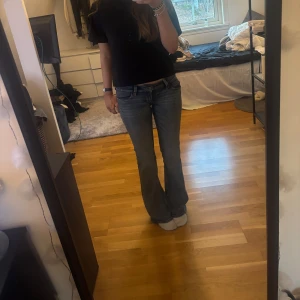 Blå bootcut jeans - Säljer ett par klassiska blå bootcut jeans. De har en snygg passform med låg midja och är perfekta för en avslappnad stil. Jeansen har en dragkedja och knappar framtill.