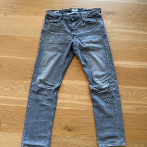 Grå jeansbyxor - Säljer ett par grå jeansbyxor med en relaxed passform. Byxorna har en klassisk femficksdesign och är perfekta för en avslappnad stil. De har en dragkedja och knapp framtill.